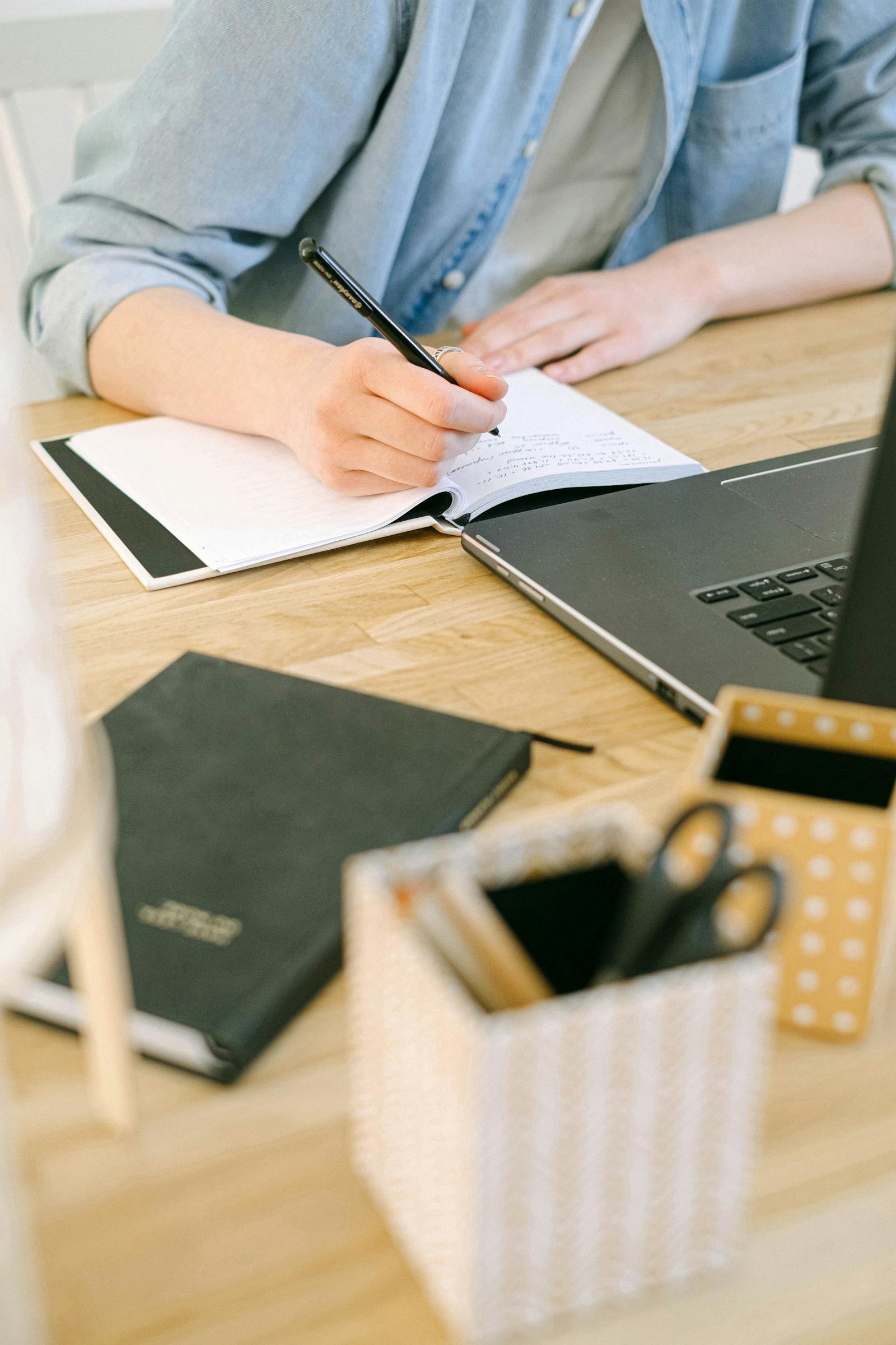 Person writing in a notebook beside a laptop